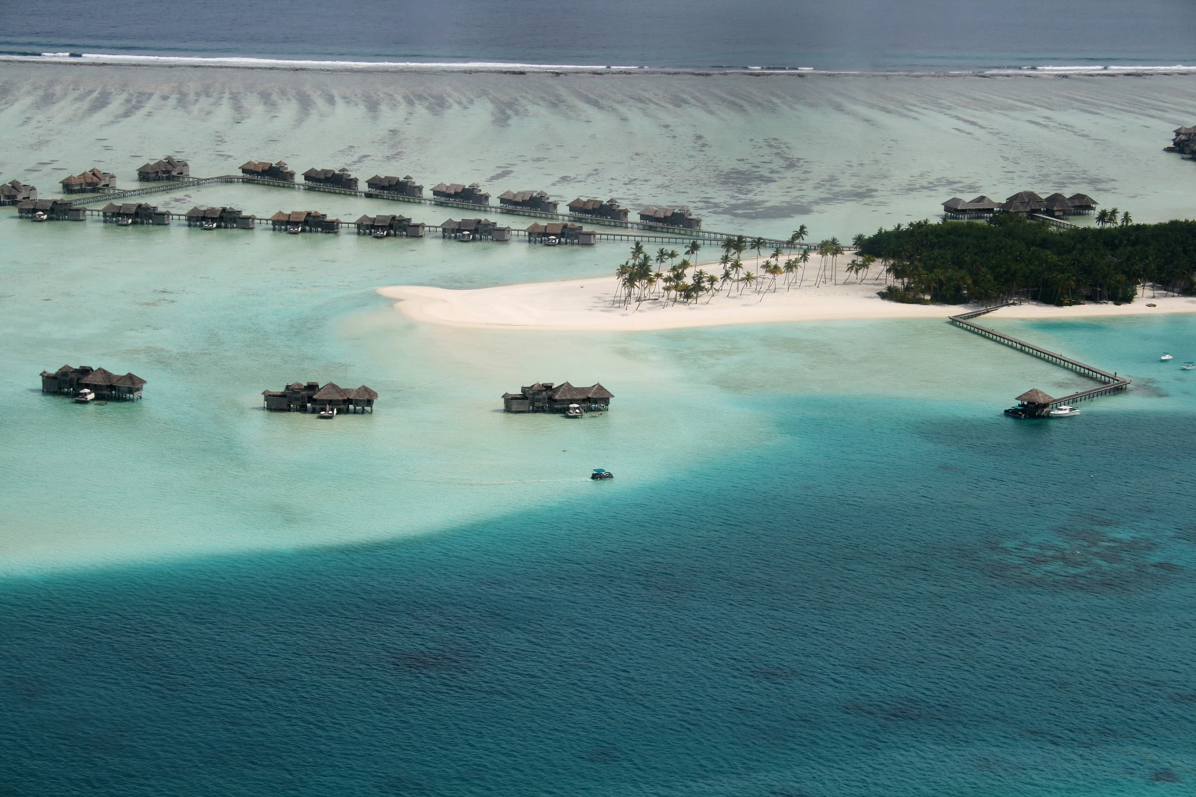 Luftaufnahme einer maledivischen Resortinsel mit Wasservillen, Stegen, Strand und Riff