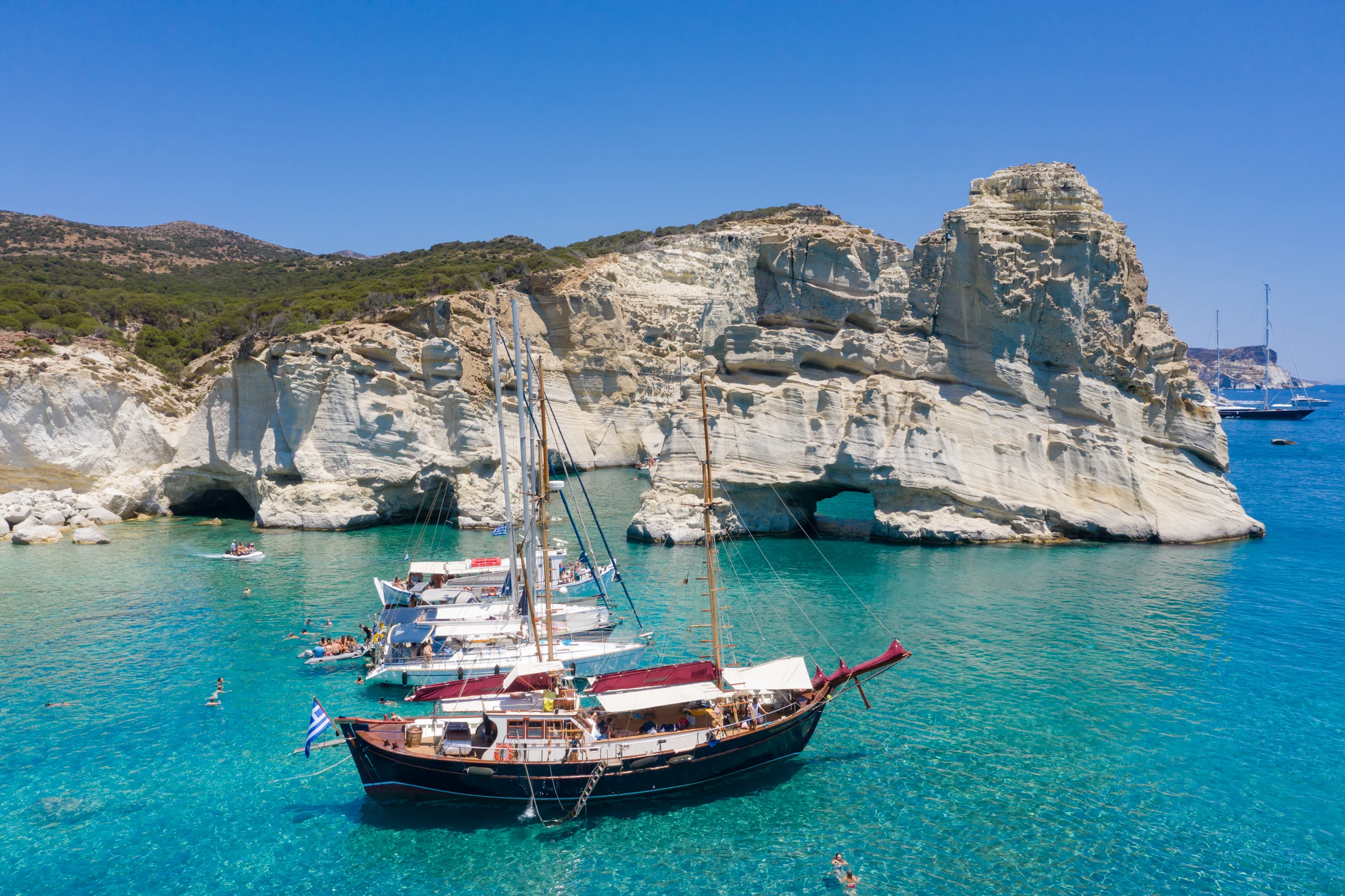 Several yachts and swimmers beside Kleftiko's pale cliffs on Milos