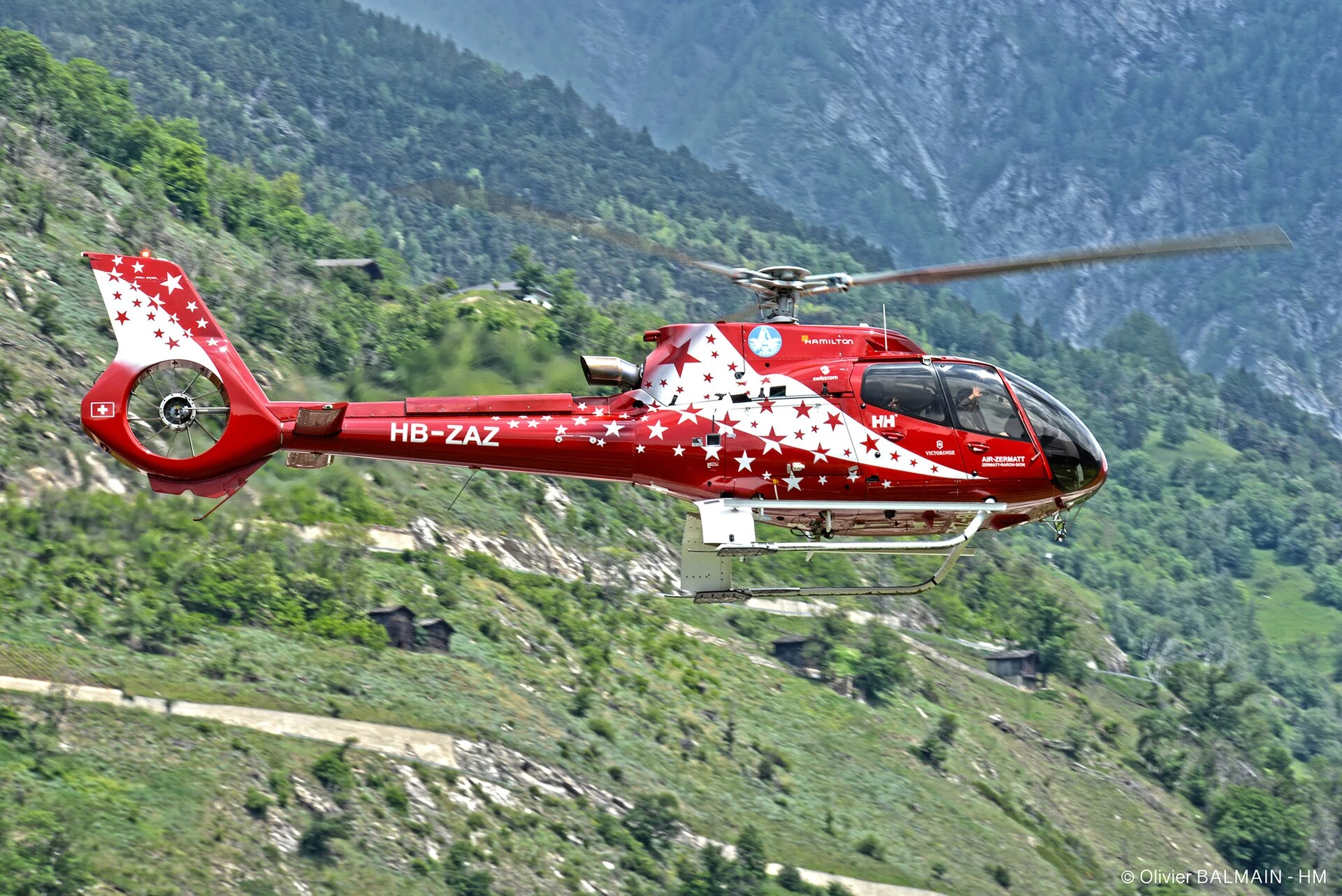 Air Zermatt H130 HB-ZAZ in flight against an Alpine slope