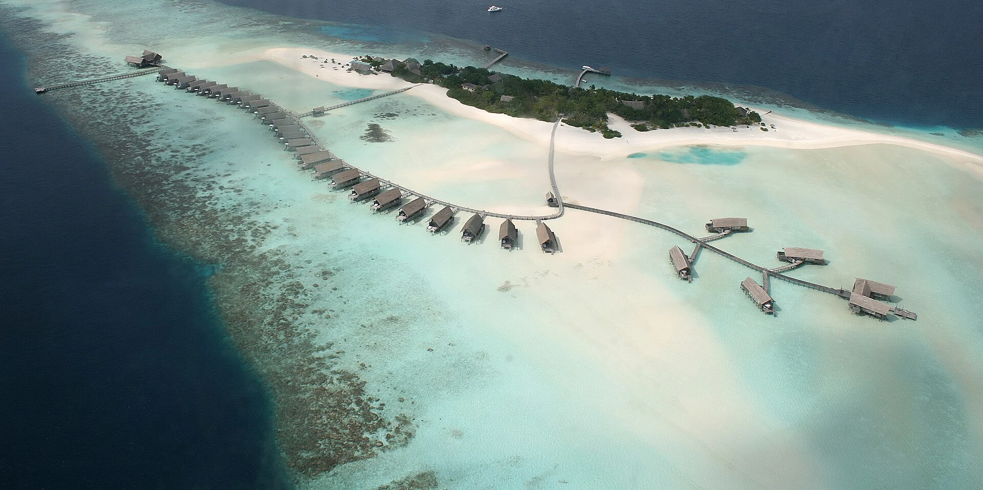 Maldivian resort island with pale lagoon, reef edge and deep outer water seen from above