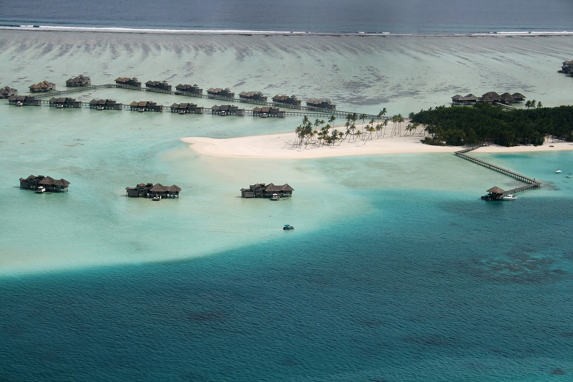 Luftbild einer maledivischen Insel mit Sandbank, flacher Lagune, Riffkante und Wasservillen