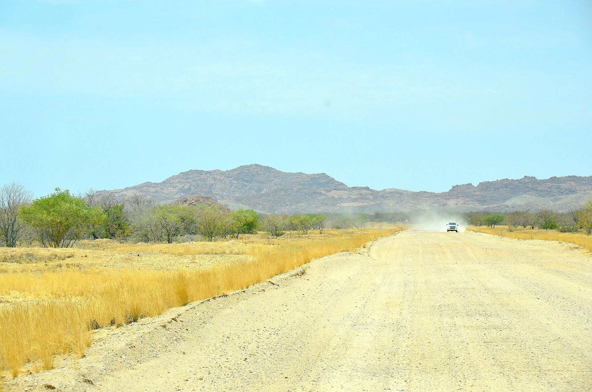 Reale breite Schotterstrasse in der Kunene-Region Namibias mit Staubfahne eines Fahrzeugs