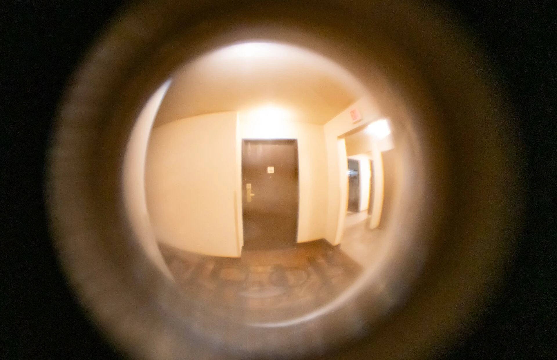 View through a hotel-room door peephole into a corridor