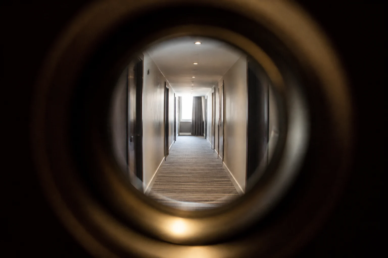 View through a hotel-room door peephole into a corridor
